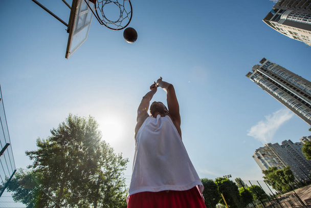 Bottom view of african american man throwing ball in basketball hoop outdoors  - Фото, зображення