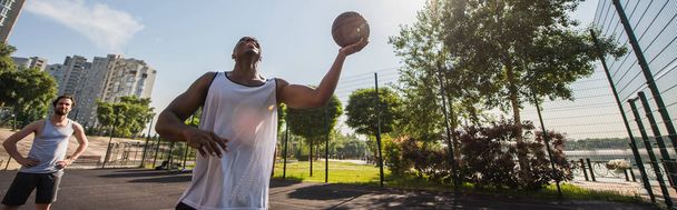 Fröhlicher Mann hält Basketballball neben Freund auf Spielplatz  - Foto, Bild