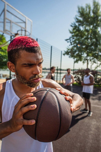 Африканський спортсмен з пофарбованим волоссям тримає баскетбольний м'яч на ігровому майданчику.  - Фото, зображення
