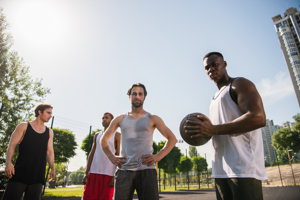 Vue à angle bas des joueurs de basket interracial regardant la caméra à l'extérieur  - Photo, image