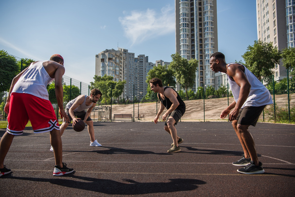 Multiethnic sportsmen playing basketball on playground outdoors  - Фото, изображение