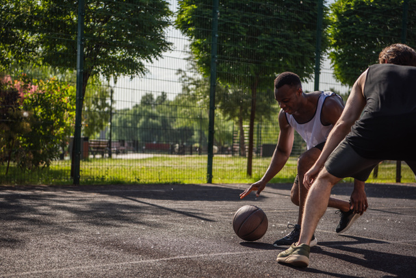 Afričtí američtí sportovci hrát streetball poblíž přítele na hřišti  - Fotografie, Obrázek