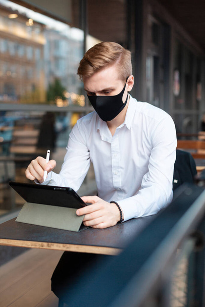 Egy fiatal szőke férfi maszkban dolgozik egy városi kávézóban. - Fotó, kép