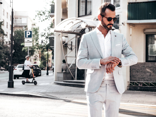 Portrait of handsome confident stylish hipster lambersexual model.Modern man dressed in elegant white suit. Fashion male posing in the street background in Europe city at sunset. In sunglasses - Foto, Imagem