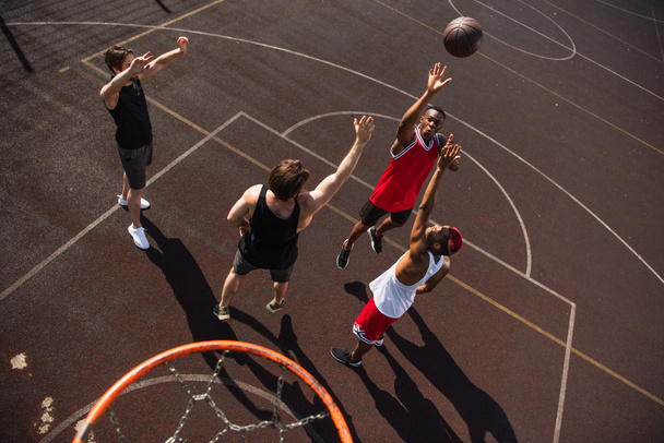 Overhead view of multiethnic sportsmen jumping while playing streetball - 写真・画像
