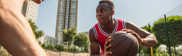 Focused african american sportsman holding basketball ball near blurred player, banner  - Fotó, kép