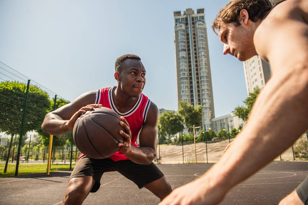 Concentrato giocatore afroamericano che tiene palla da basket vicino amico durante la competizione  - Foto, immagini