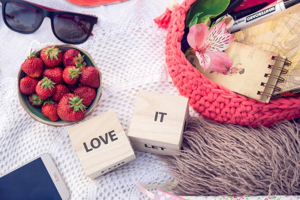Макет srtawberries в миске, солнцезащитные очки, надпись "люблю его", розовый ящик с альбомами эскизов, ручки и цветок, все на крючковую текстуру. Летняя творческая работа и концепция планирования. - Фото, изображение