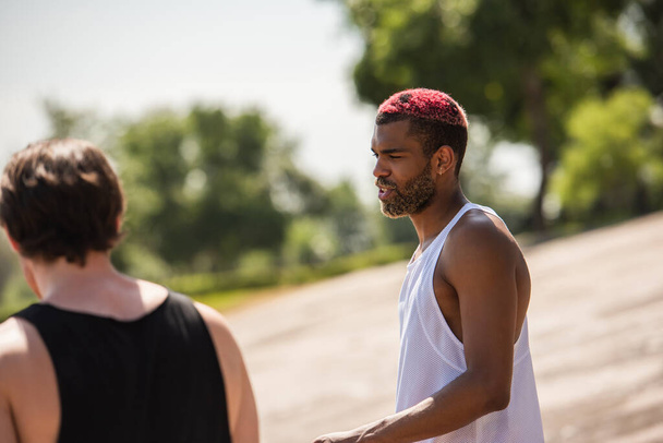 Açık havada bulanık bir arkadaşın yanında konuşan Afrikalı Amerikalı sporcu.  - Fotoğraf, Görsel