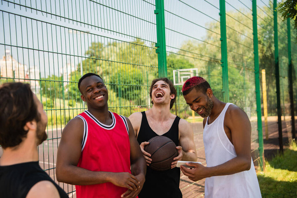 Positivi sportivi multietnici con pallacanestro e smartphone all'aperto  - Foto, immagini