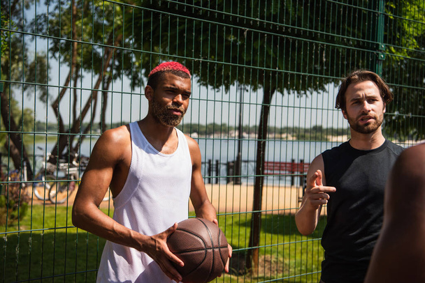 African american basketball player standing near friends talking outdoors  - 写真・画像