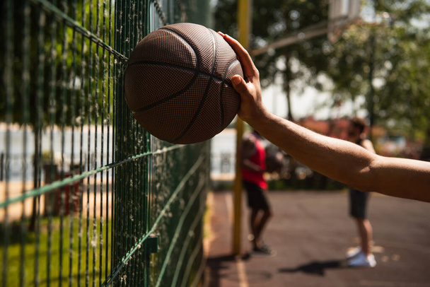 Cropped view of african american sportsman holding basketball ball near fence outdoors  - Φωτογραφία, εικόνα