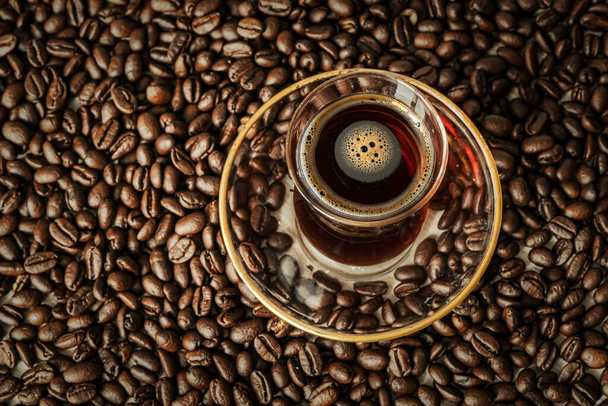 Szklany kubek w tradycyjnym tureckim stylu z czarną kawą stoi na leżącej na stole ziarnie kawy. Pyszny napój energetyczny. - Zdjęcie, obraz