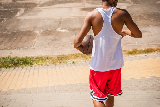 Cropped view of african american sportsman with basketball ball walking outdoors  - Foto, afbeelding