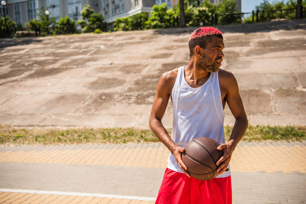 Side view of african american sportsman holding basketball ball outdoors  - Foto, Imagem