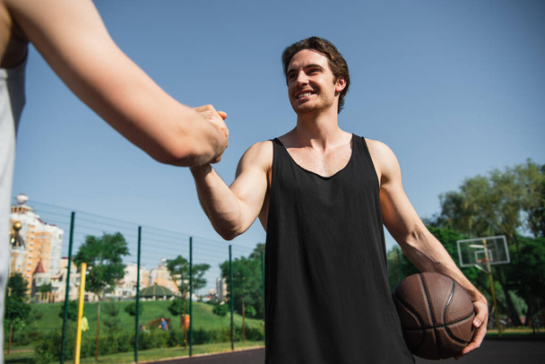 Low angle view of smiling sportsman with basketball ball greeting with friend  - Fotó, kép