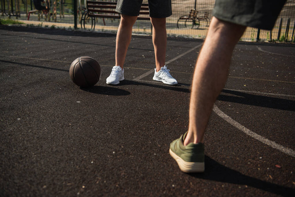 Cropped view of sportsmen standing near basketball ball on court  - 写真・画像