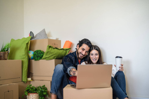 Onnellinen nuori pari siirtymässä uuteen kiinteistön taloon, kun käytät kannettavaa tietokonetta ostoksia varten verkossa - Valokuva, kuva