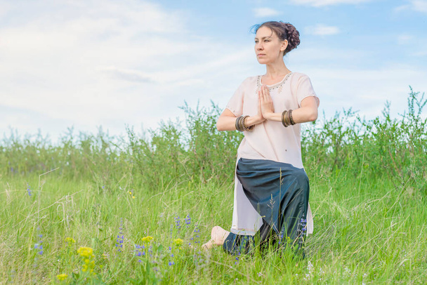 Mooie jonge vrouw oefent buiten yoga. Staat op één knie, vouwde haar handpalmen voor haar en kijkt opzij. - Foto, afbeelding