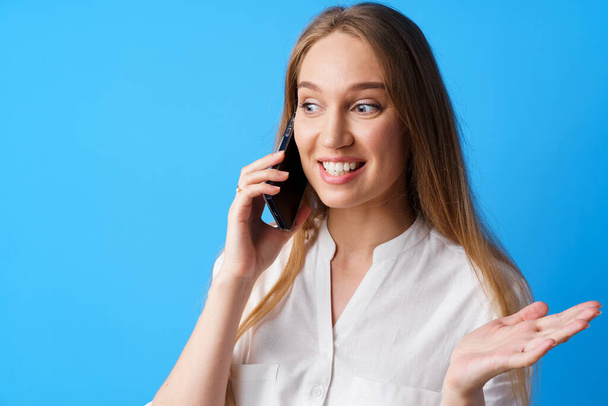 Happy hymyilevä nuori nainen puhuu puhelimessa sinistä taustaa vasten - Valokuva, kuva