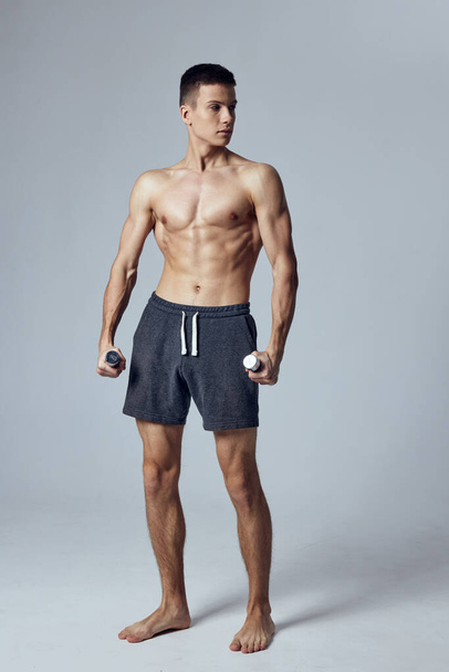 hombre deportivo en pantalones cortos con pesas en las manos ejercicios de entrenamiento estudio - Foto, Imagen