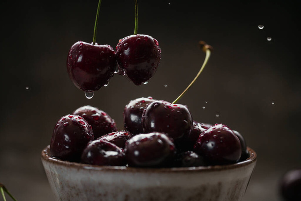 Close up of ripe juicy sweet cherries with water drops in a ceramic bowl on dark background - Fotó, kép
