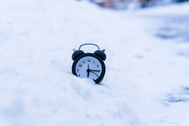 Alarm clock in a snowy winter close-up. The concept of the winter time. Copy space - Fotoğraf, Görsel
