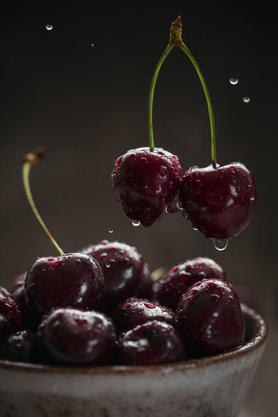 Ripe juicy sweet cherries with water drops in a ceramic bowl on dark background. Flying cherry - Fotografie, Obrázek