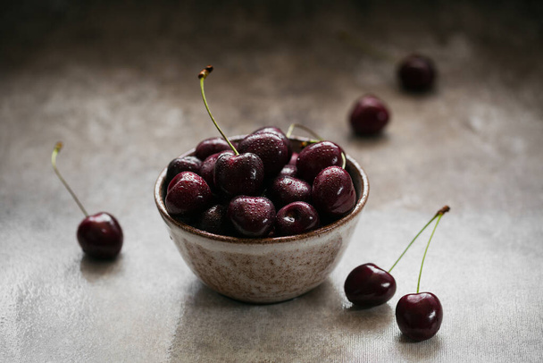Ripe juicy sweet cherries with water drops in a ceramic bowl on dark background - Fotó, kép