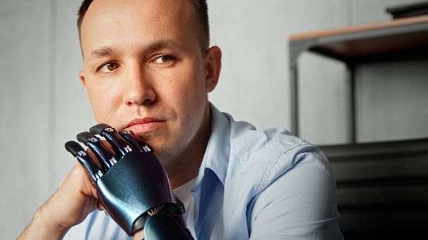 Vakava cyborg vammainen mies bio proteesi mielestä pitämällä päänsä kädet istuu hämärtynyt kirjahylly - Valokuva, kuva