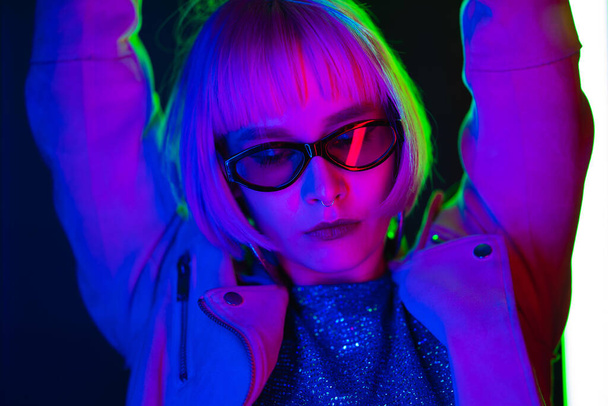 Amazing woman with dyed pink hairstyle dancing on led-colorful neon lamps background. Charming lady, night life concept. Modern pop outfit, influencer lifestyle. - Foto, afbeelding