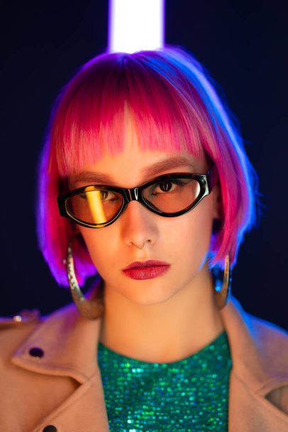 Portrait of glamorous woman on party under glowing neon light. Nightclub, trendy outfit. Teenager, zoomer Z-generation. Lady with sunglasses and massive hoops earrings - Photo, image