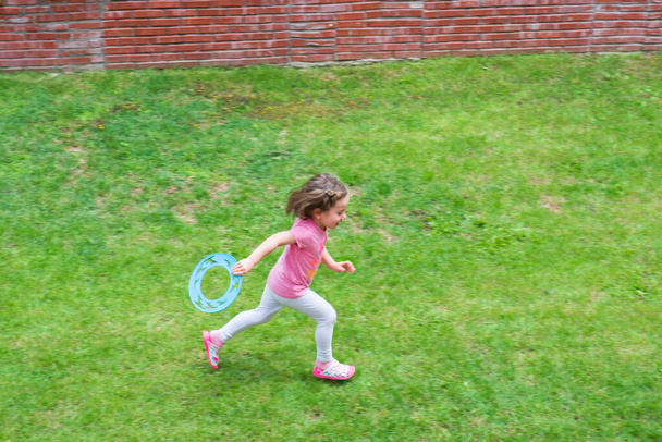 little girl is playing frisbee on the grass in the garden of their house. Selective Focus Girl. - Photo, Image