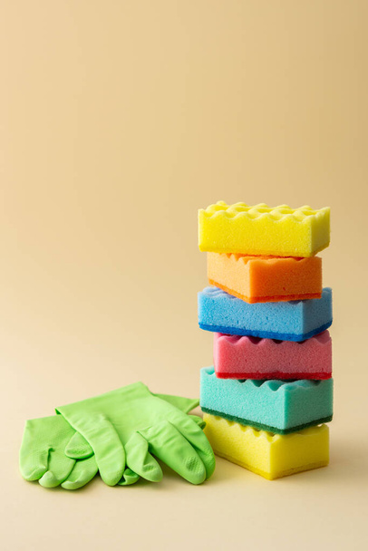 Pila de esponjas lavavajillas multicolores y guantes de goma verde sobre fondo beige neutro, hogar de cocina y concepto de limpieza - Foto, imagen