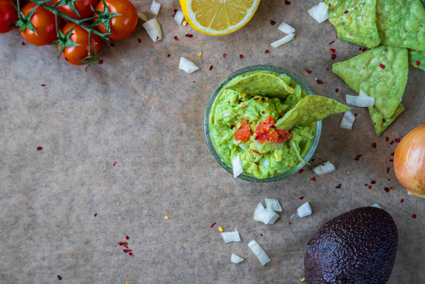 Horní pohled na čerstvé domácí guacamole dip se zelenou avokádovou příchutí, tortilla chipsy. Tradiční mexické jídlo bez lepku. Třešňová rajčata, cibule a citron v pozadí na rustikální látky. Textový prostor - Fotografie, Obrázek