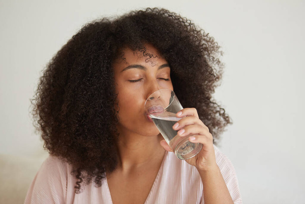 Egy fiatal fekete hölgy egy pohár tiszta ásványvizet tart, javítja az egészséget és a jólétet., - Fotó, kép
