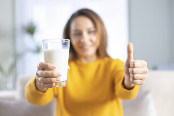 Mujer joven sosteniendo un vaso de leche haciendo signo ok, pulgar hacia arriba con los dedos, señal excelente - Foto, Imagen