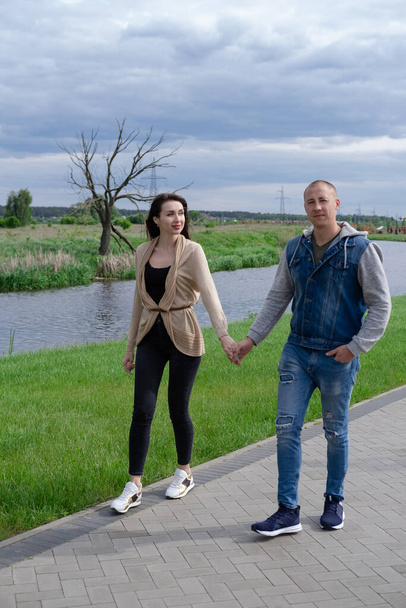 lovely happy couple walking in park by the river holding hands. brunette woman and bald man. wife and husband. successful marriage, true love. romantic walk on a date. - Photo, Image