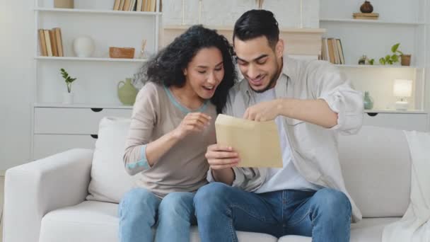 Španělský hispánec ženatý pár etnická rodina sedět na pohovce doma obdrží dopis poštou oznámení od banky s dobrou zprávou číst papír vyhrát loterie peníze radovat oslavit výkřik štěstí - Záběry, video