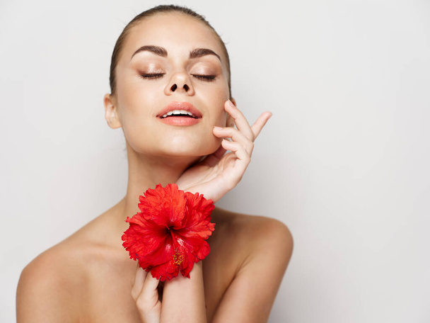 όμορφη γυναίκα με γυμνούς ώμους κλειστά μάτια φως φόντο κόκκινο λουλούδι - Φωτογραφία, εικόνα