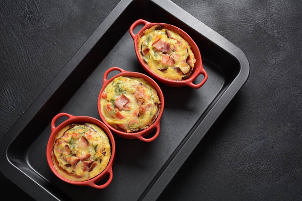 Omelette con pancetta, parmigiano grattugiato e verdure in cocotte ceramiche su teglia da forno. Colazione gustosa - Foto, immagini