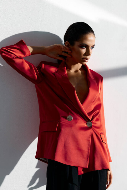 magabiztos nő piros kabát áll közel a fal belső szoba ruha divat stílus - Fotó, kép