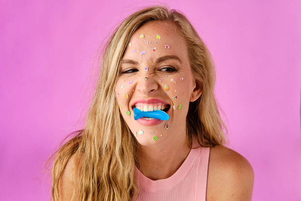 Pretty blonde girl with stickers on her face biting a candy on a pink background - Foto, afbeelding