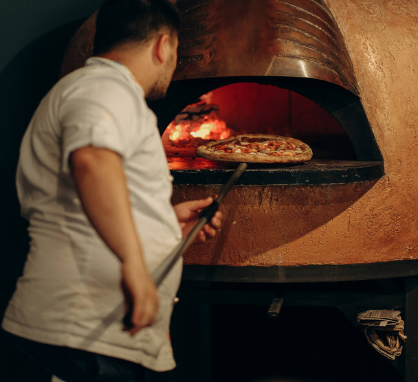 De chef bereidt pizza in een houtoven. Pizza koken. De kok zet de pizza in de oven. - Foto, afbeelding