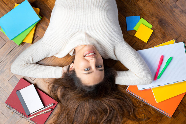 Relaxed young woman lying on the floor and surrounded by books. Exam period for high school students - Φωτογραφία, εικόνα