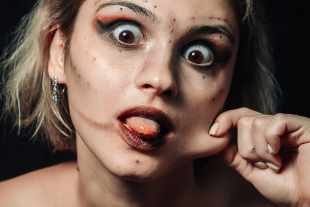 Retrato de close-up de uma mulher em um fundo preto. Menina com maquiagem manchada mostra língua - Foto, Imagem