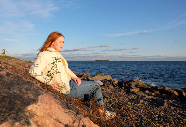 Beautiful girl body positive looking ahead on rocks seaside background in autumn season - Zdjęcie, obraz