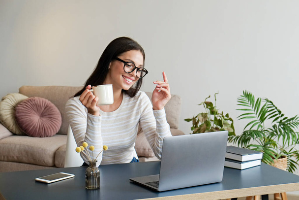 Online education concept. Young beautiful brunette woman wearing eyeglasses taking part in a group video call. Portrait of female college student studying at home. Close up, copy space, background. - Foto, Imagem