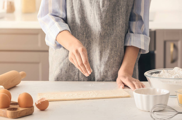 Woman sprinkling dough with flour on kitchen table - Photo, Image