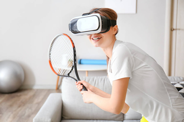 Молодая женщина в очках виртуальной реальности играет в теннис дома - Фото, изображение